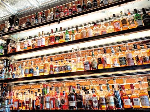 Multiple rows of spirit bottles on backlit bar shelves against an exposed brick wall