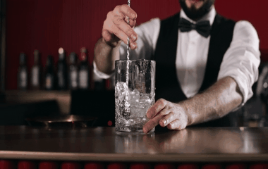 An animated GIF of a bartender in a bow tie stirring a cocktail in a mixing glass with a bar spoon