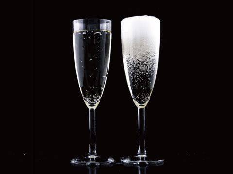 Two tall Champagne flutes side by side against a black background, one with clear sparkling wine and one coated in frost