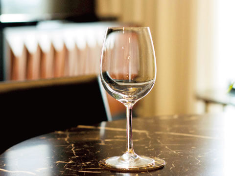 An empty stemmed wine glass with a rounded bowl, standing on a dark marble table in a softly lit room