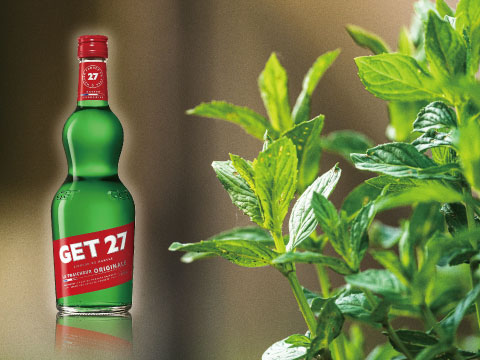 A bottle of Get 27 green mint liqueur beside fresh mint leaves, showcasing its vivid green color