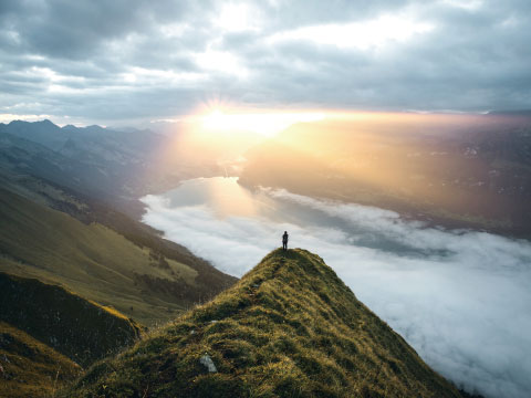 A person standing on a mountain ridge overlooking a valley filled with clouds during a golden sunrise
