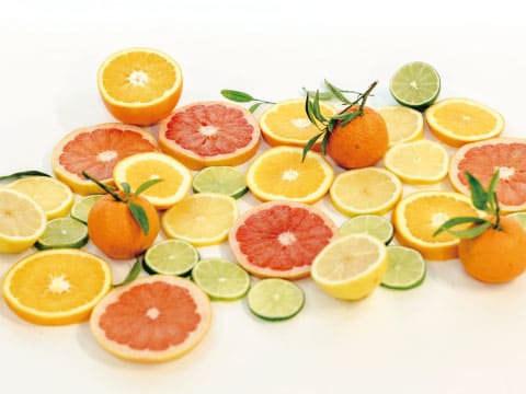 Sliced oranges, grapefruit, lemons, limes, and mandarins are arranged together on a white background.