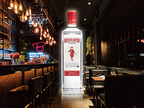 A bottle of Beefeater London Dry Gin displayed on a bar counter, with warm pendant lighting and booth seating in the background