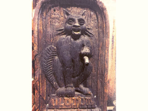 A weathered wooden carving of a black cat holding a bottle, inscribed "Old Tom," historically used as a gin shop sign