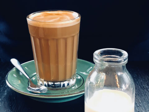 A creamy Eggnog-style drink served in a ribbed glass on a green saucer, with a small glass milk bottle beside it