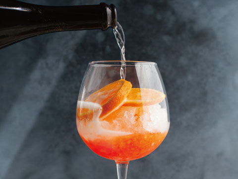 Sparkling wine being poured over crushed ice into a wine glass, garnished with fresh orange slices, in classic Cobbler style