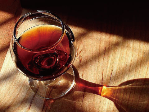 A deep red Sangaree-style wine drink served in a brandy snifter, viewed from above with warm sunlight casting shadows on a wooden table