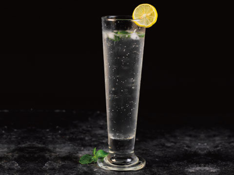 A clear sparkling Sonic-style cocktail in a tall footed glass, garnished with a lemon wheel and fresh mint, set against a dark background