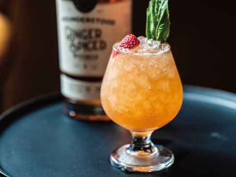 A crushed-ice Daisy cocktail in a snifter glass, garnished with a fresh strawberry and mint sprig, with a whiskey bottle in the background