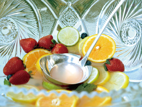 A crystal Punch bowl filled with citrus slices and strawberries, with a silver ladle used to serve the communal cocktail