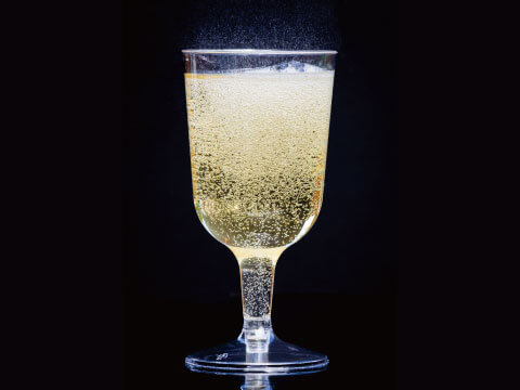 A pale golden Fizz-style cocktail with rising carbonation bubbles, served in a stemmed glass against a dark background