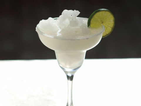 A frozen Margarita topped with crushed ice, served in a salt-rimmed margarita glass and garnished with a lime wheel