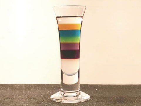 A tall shot glass with a Pousse Café-style rainbow of distinct, unmixed liqueur layers stacked by density
