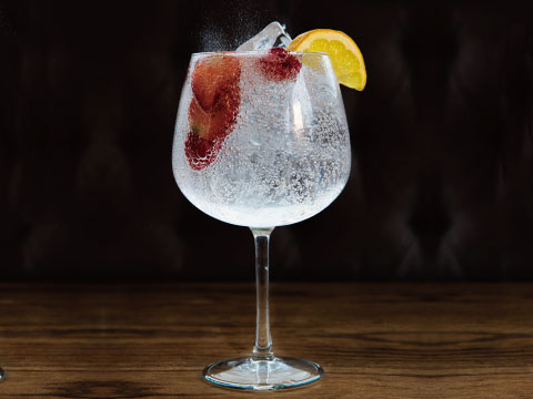 A sparkling Rickey cocktail served over ice in a wine glass, garnished with fresh berries and a lemon wedge