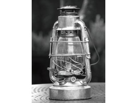 A metal-framed hurricane lamp with a glass globe sits on a table in a black-and-white photo.
