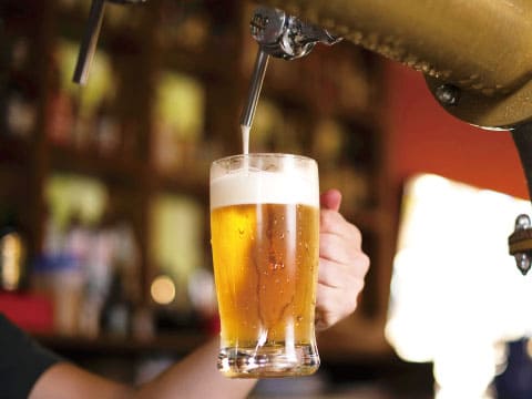 A glass being filled with golden beer and foam from a bar tap, held by a hand at a dimly lit bar
