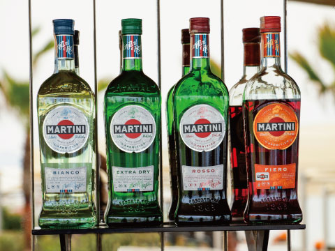 Four Martini vermouth bottles lined up on a shelf, showing Bianco, Extra Dry, Rosso, and Fiero varieties
