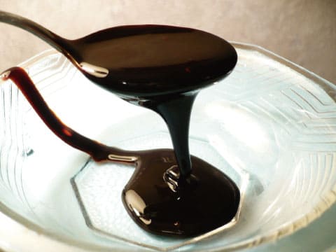 Thick dark molasses drips from a spoon into a glass bowl.