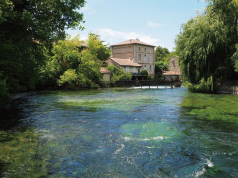 A clear river flows past a distillery building surrounded by trees in the countryside.