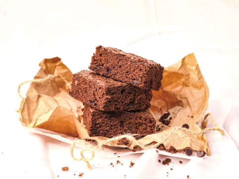 Three stacked chocolate brownies with chocolate chips, resting on crumpled parchment paper