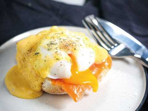 A poached egg with runny yolk over smoked salmon and hollandaise sauce, served on an English muffin