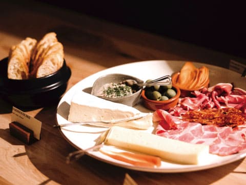 A charcuterie plate with brie, cheese, prosciutto, olives, and dip, served with bread on a wooden table