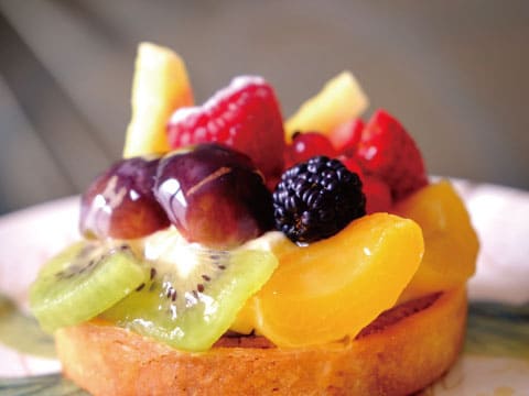 A fruit tart topped with kiwi, grapes, berries, and peach slices over a creamy custard base