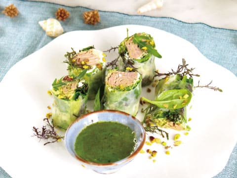 Fresh spring rolls filled with herbs and meat, sliced and arranged on a white plate with a bright green dipping sauce