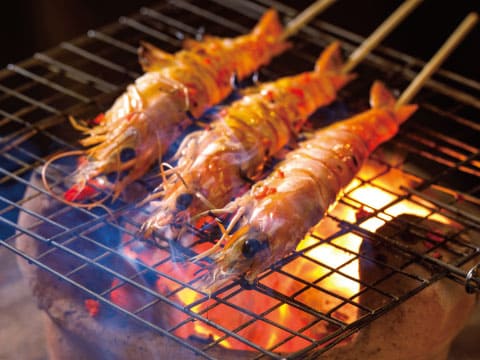 Whole shrimp skewers grilling over an open charcoal fire on a wire rack