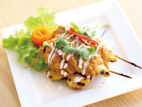 Grilled chicken satay skewers drizzled with peanut sauce, garnished with cilantro and served with a side salad