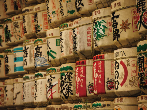 Rows of decorative sake barrels (komodaru) wrapped in straw with Japanese brewery labels, representing fermented alcohol made through multiple parallel fermentation