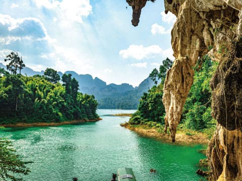 A turquoise lake winds through a tropical jungle landscape framed by towering limestone cliffs and forested mountains.