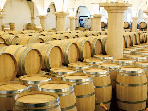 Rows of oak barrels fill a stone-arched wine cellar, used for aging wine and spirits.