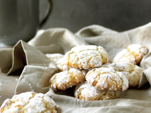 A pile of Amaretti cookies dusted with powdered sugar, resting on a linen cloth