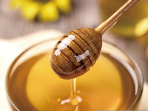 Golden honey dripping from a wooden honey dipper into a glass bowl, with soft warm lighting