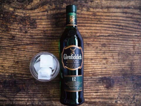 A bottle of Glenfiddich 12 Year Old single malt Scotch whisky beside a glass of whisky on ice