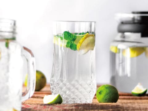Cut-crystal glass filled with a clear vodka highball, garnished with lime wedges and fresh mint on a wooden table