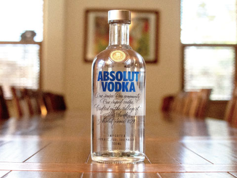 Absolut Vodka bottle standing on a wooden dining table with a bright window backdrop