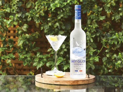Grey Goose vodka bottle beside a martini glass garnished with lemon peel on an outdoor wooden table