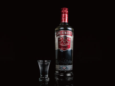 Smirnoff triple-distilled vodka bottle beside a filled shot glass against a dark backdrop