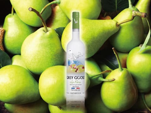 Grey Goose La Poire pear-flavored vodka bottle set against a pile of green pears