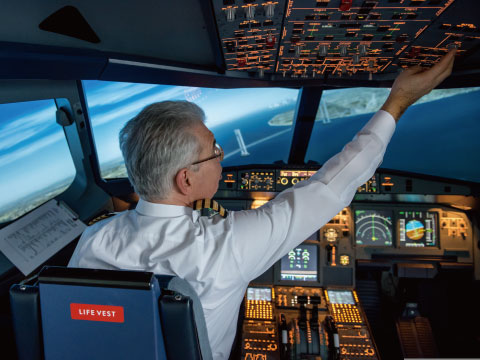 A pilot in uniform reaching up to adjust overhead controls in an aircraft cockpit simulator
