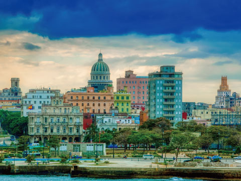 Colorful historic buildings and a domed capitol building along the Havana waterfront under a dramatic sky