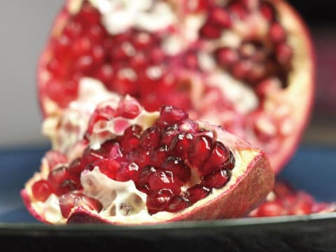 A pomegranate is split open, revealing clusters of glistening red seeds inside.