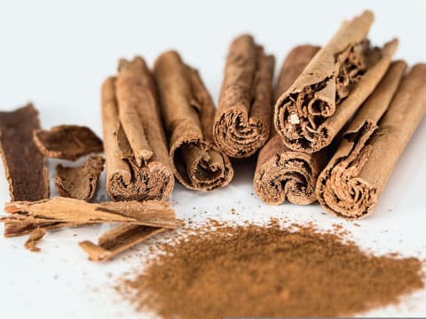 Rolled cinnamon sticks and bark pieces are arranged beside a pile of ground cinnamon powder.
