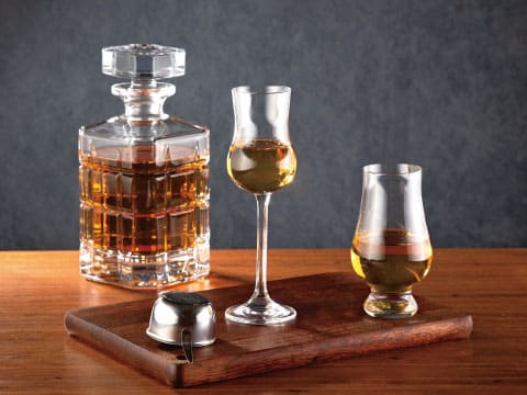A crystal decanter and two tasting glasses filled with amber-colored spirit, arranged on a wooden tray