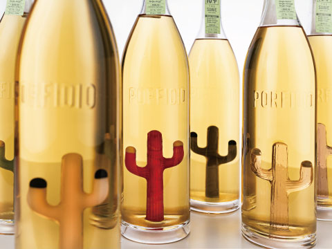 Several Porfidio tequila bottles lined up, each featuring a differently colored hand-blown glass cactus inside — tan, red, black, and gold