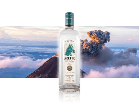 Bottle of Arette Blanco tequila featuring a horse logo, displayed against a backdrop of clouds and an erupting volcano
