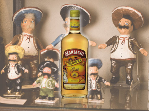 A bottle of Mariachi Gold tequila displayed on a shelf surrounded by small decorative figurines dressed in traditional mariachi costumes and sombreros
